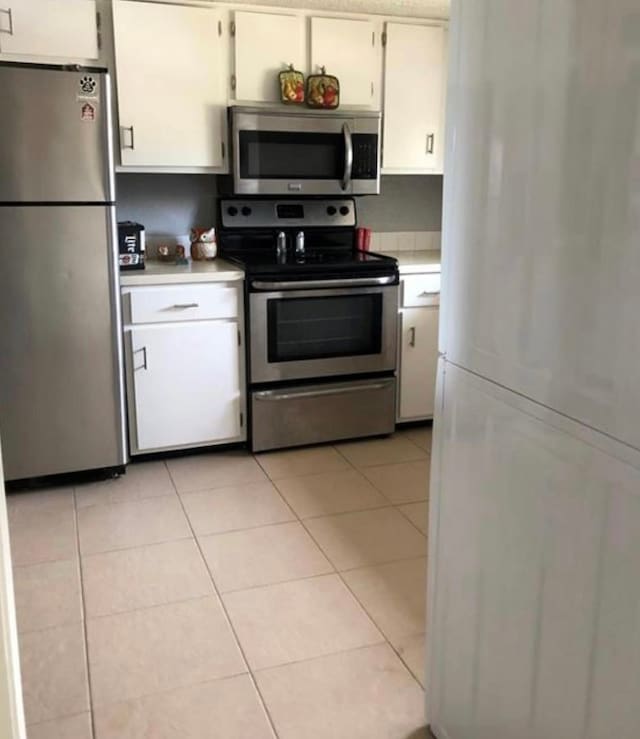 kitchen featuring appliances with stainless steel finishes, light tile flooring, and white cabinetry