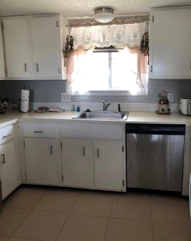 kitchen with sink, white cabinetry, light tile floors, and stainless steel dishwasher