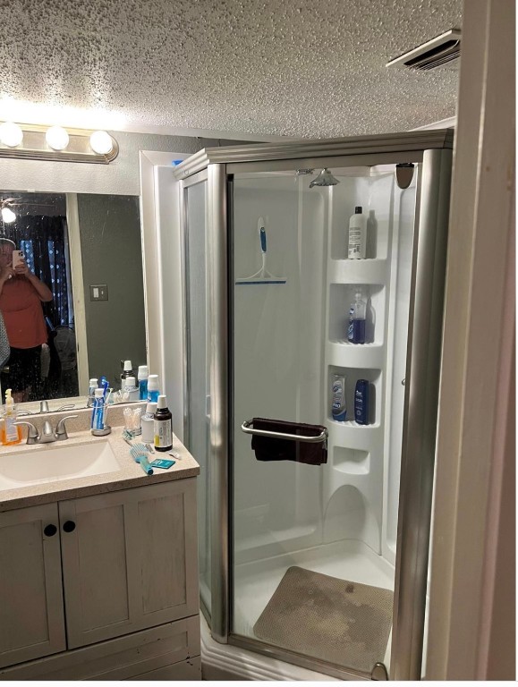 bathroom featuring walk in shower, vanity with extensive cabinet space, and a textured ceiling