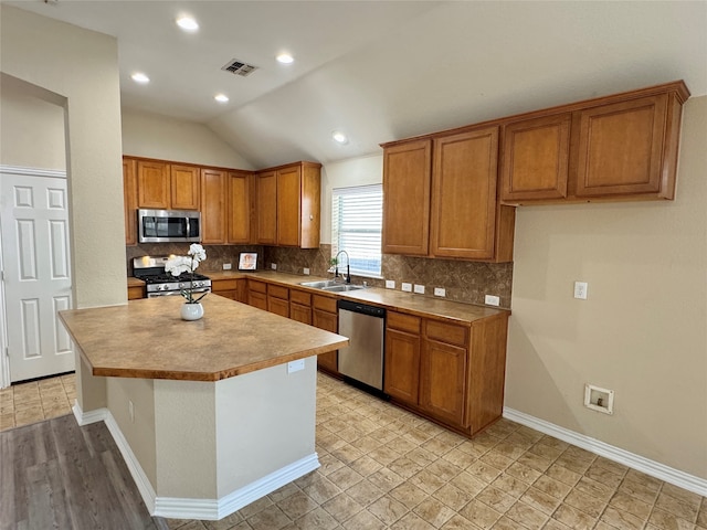 kitchen featuring sink, backsplash, lofted ceiling, a kitchen island, and appliances with stainless steel finishes