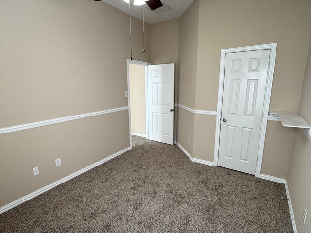 unfurnished bedroom featuring ceiling fan, a towering ceiling, and dark colored carpet