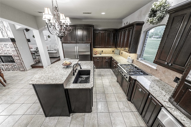 kitchen featuring light stone countertops, appliances with stainless steel finishes, tasteful backsplash, an island with sink, and light tile floors