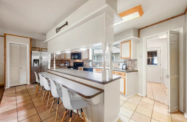 kitchen featuring a kitchen breakfast bar, white cabinetry, black appliances, light tile floors, and tasteful backsplash