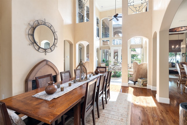 dining space featuring hardwood / wood-style flooring, ceiling fan with notable chandelier, and a towering ceiling