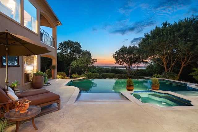 pool at dusk with a patio area and an in ground hot tub