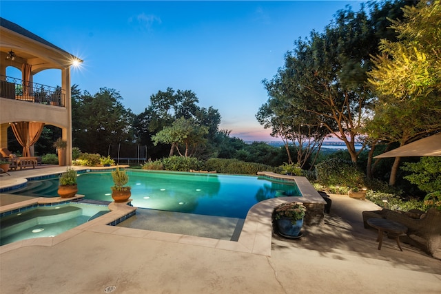 pool at dusk featuring a patio area, an in ground hot tub, and a trampoline