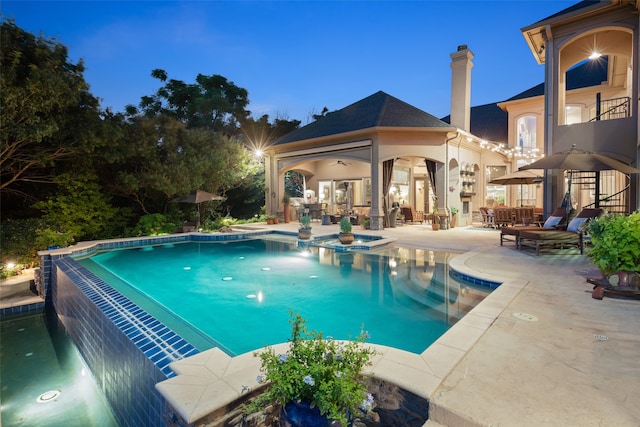 pool at dusk featuring ceiling fan and a patio area