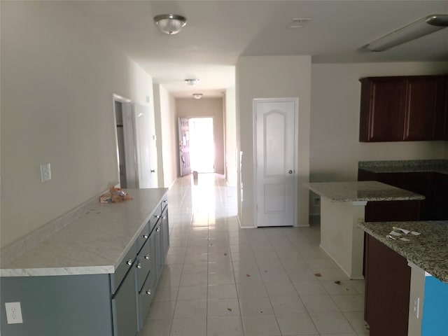 kitchen with dark brown cabinets, light tile floors, a kitchen island, and light stone countertops