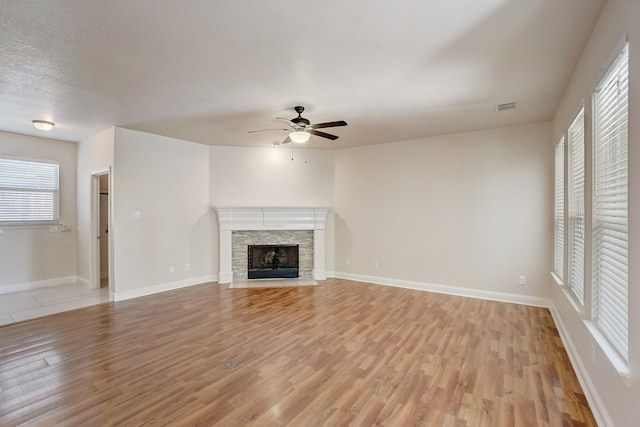 unfurnished living room with a healthy amount of sunlight, a fireplace, ceiling fan, and light hardwood / wood-style floors