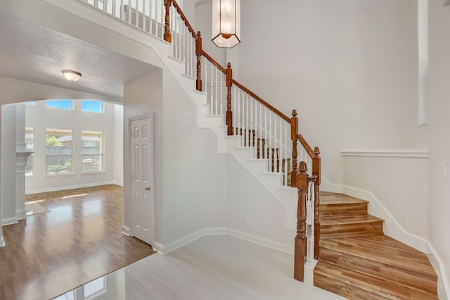 stairway with a textured ceiling, a high ceiling, and hardwood / wood-style floors