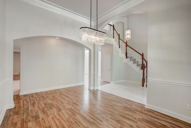 unfurnished dining area with an inviting chandelier, crown molding, light wood-type flooring, and a high ceiling