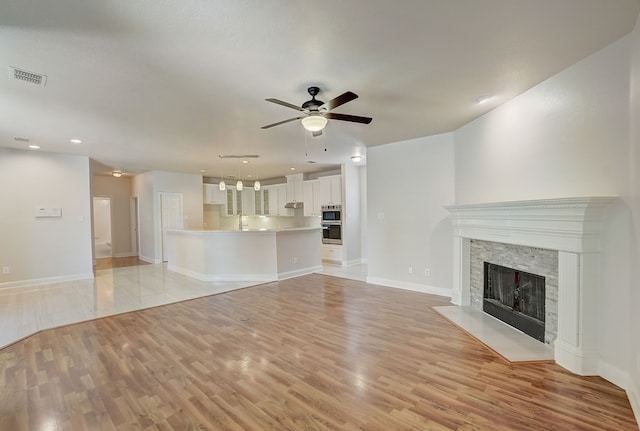 unfurnished living room with sink, ceiling fan, light hardwood / wood-style floors, and a stone fireplace