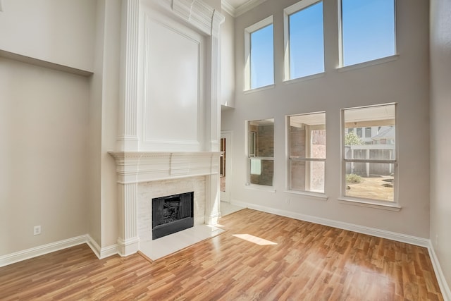 unfurnished living room with a fireplace, light hardwood / wood-style flooring, a towering ceiling, and crown molding