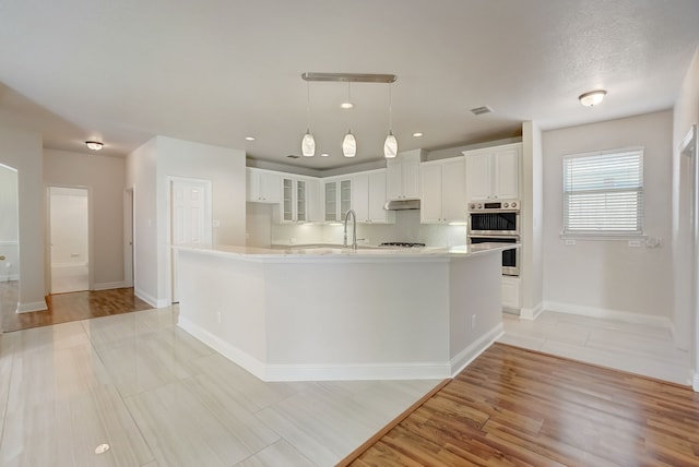 kitchen with decorative light fixtures, tasteful backsplash, light hardwood / wood-style flooring, white cabinetry, and stainless steel double oven