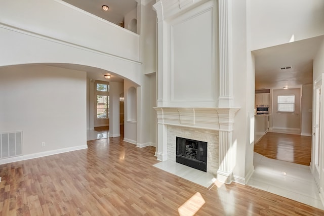 unfurnished living room with a towering ceiling, a fireplace, and light wood-type flooring