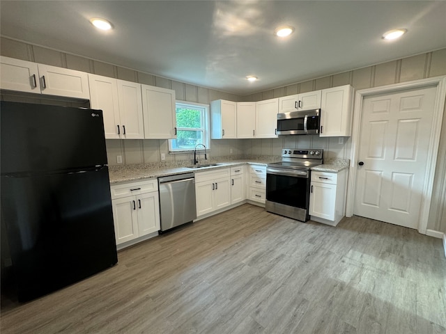 kitchen with appliances with stainless steel finishes, sink, light hardwood / wood-style floors, white cabinetry, and light stone countertops