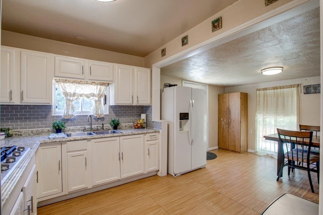 kitchen featuring white fridge with ice dispenser, sink, tasteful backsplash, and white cabinetry