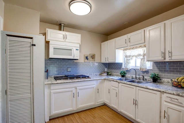 kitchen with stainless steel gas cooktop, white cabinets, light hardwood / wood-style flooring, sink, and tasteful backsplash