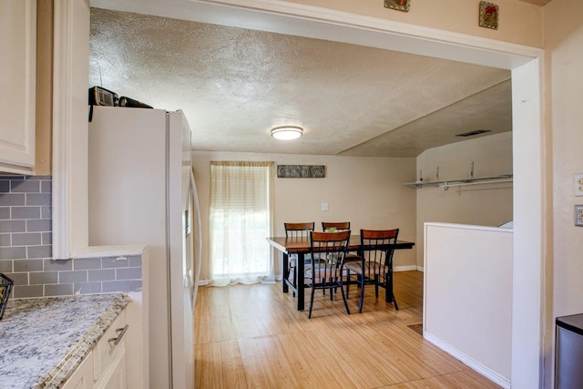 kitchen with white refrigerator, light hardwood / wood-style floors, tasteful backsplash, and white cabinets