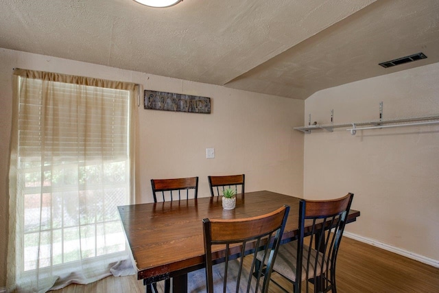 dining space with hardwood / wood-style floors, vaulted ceiling, and a textured ceiling