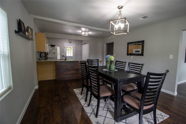 dining area featuring sink, dark wood-type flooring, and an inviting chandelier