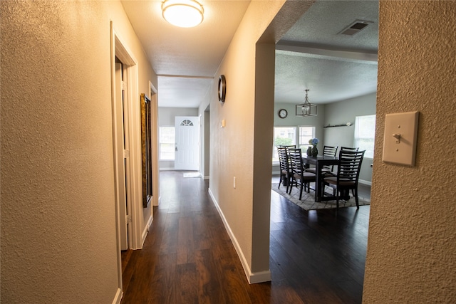 hall featuring a textured ceiling, dark hardwood / wood-style flooring, and an inviting chandelier