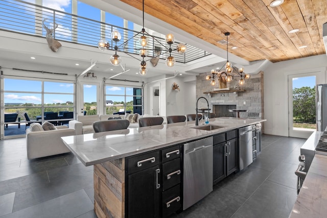 kitchen featuring wood ceiling, appliances with stainless steel finishes, a kitchen island with sink, decorative light fixtures, and a chandelier