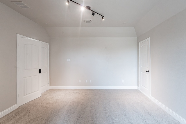 empty room with lofted ceiling, carpet flooring, and track lighting