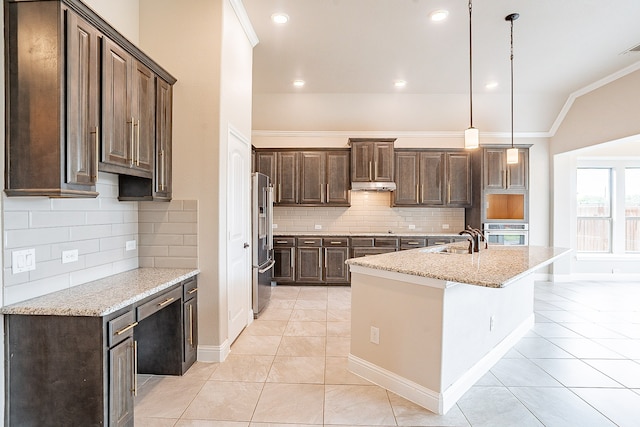 kitchen featuring a kitchen island with sink, decorative light fixtures, backsplash, appliances with stainless steel finishes, and light stone counters