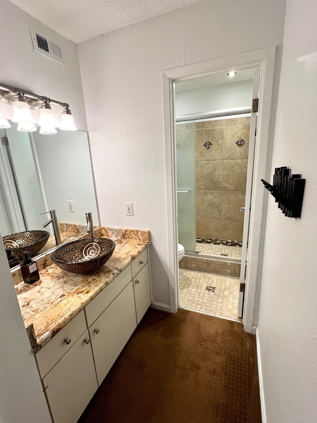 bathroom featuring a shower with door, tile patterned floors, toilet, vanity, and a textured ceiling