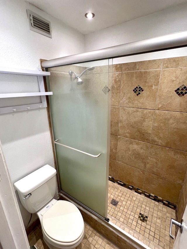 bathroom featuring a shower with door and toilet