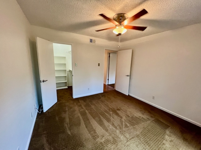 unfurnished bedroom with a closet, ceiling fan, a textured ceiling, and a walk in closet