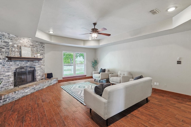 living room with dark hardwood / wood-style floors, a fireplace, a raised ceiling, and ceiling fan