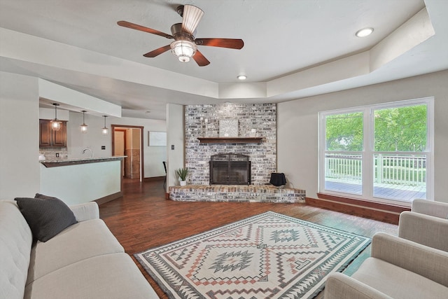 living room featuring a fireplace, ceiling fan, sink, a raised ceiling, and dark hardwood / wood-style floors