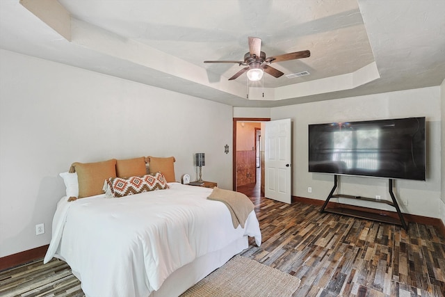 bedroom featuring ceiling fan, dark hardwood / wood-style floors, and a tray ceiling