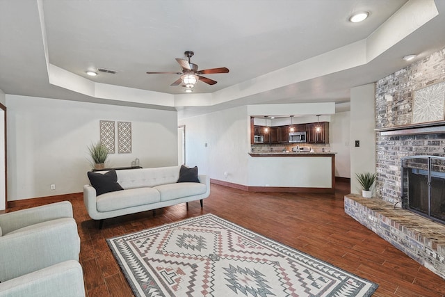 living room featuring dark hardwood / wood-style flooring, a fireplace, ceiling fan, and a tray ceiling