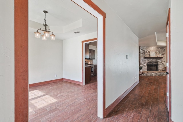 hallway featuring an inviting chandelier, brick wall, a raised ceiling, and hardwood / wood-style floors