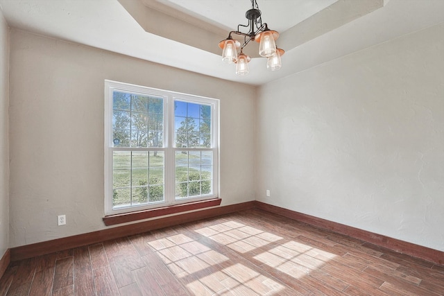 unfurnished room with an inviting chandelier, a raised ceiling, and hardwood / wood-style floors