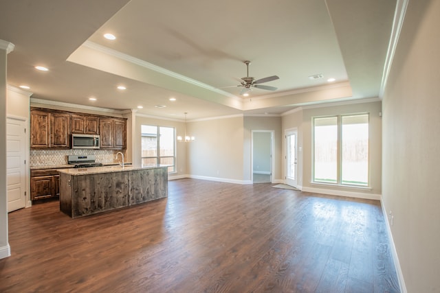 kitchen featuring an island with sink, a raised ceiling, dark wood-type flooring, and appliances with stainless steel finishes