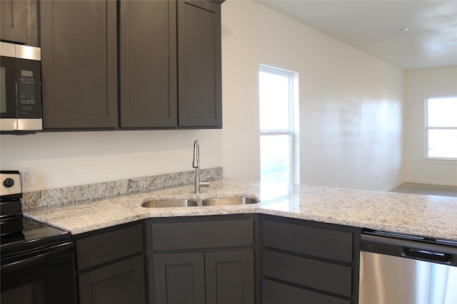 kitchen featuring light stone countertops, appliances with stainless steel finishes, kitchen peninsula, and sink