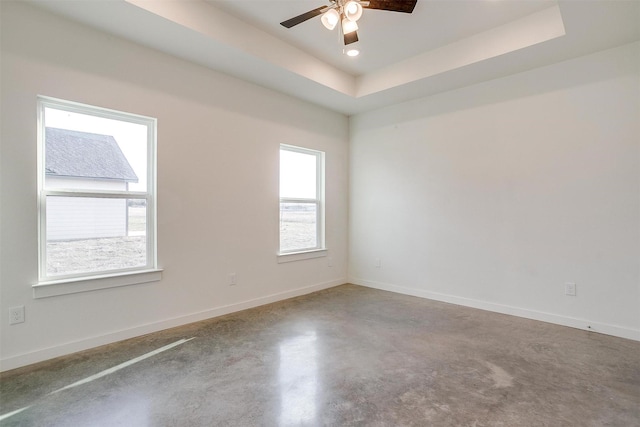 empty room featuring a raised ceiling, a healthy amount of sunlight, and concrete floors