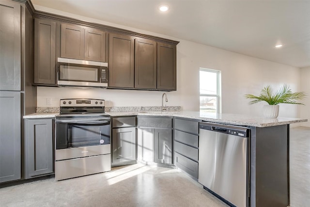 kitchen with appliances with stainless steel finishes, sink, kitchen peninsula, light stone counters, and dark brown cabinets