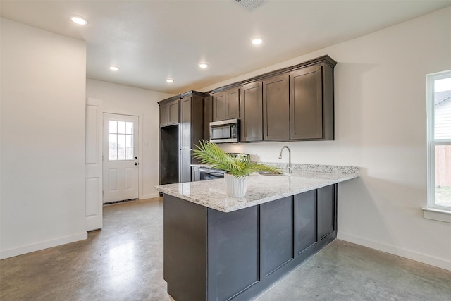 kitchen featuring light stone counters, a wealth of natural light, dark brown cabinetry, and kitchen peninsula