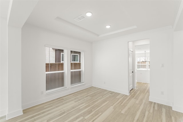 spare room featuring ornamental molding, a raised ceiling, a chandelier, and light wood-type flooring