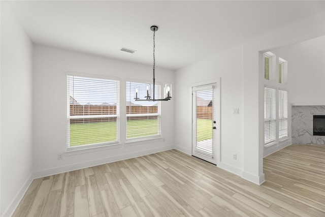 unfurnished dining area with light hardwood / wood-style flooring, a chandelier, and a fireplace