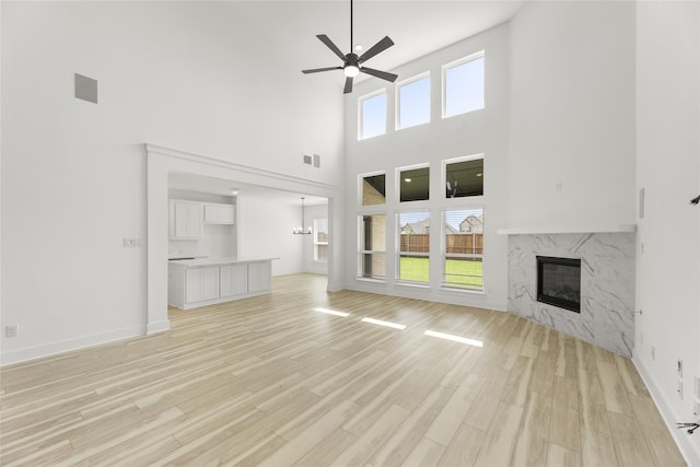 unfurnished living room featuring a fireplace, ceiling fan, light hardwood / wood-style floors, and a high ceiling