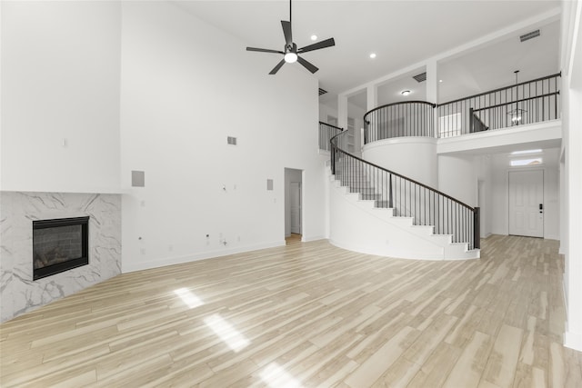 unfurnished living room with ceiling fan, a towering ceiling, light wood-type flooring, and a premium fireplace