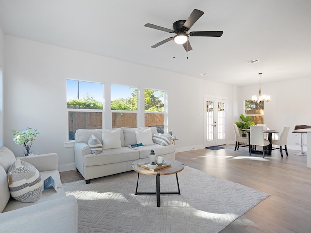 living room with ceiling fan with notable chandelier, light hardwood / wood-style flooring, and french doors