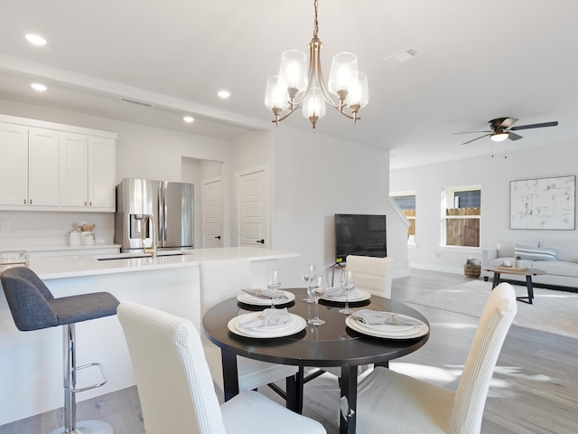 dining area with ceiling fan with notable chandelier, light hardwood / wood-style flooring, and sink