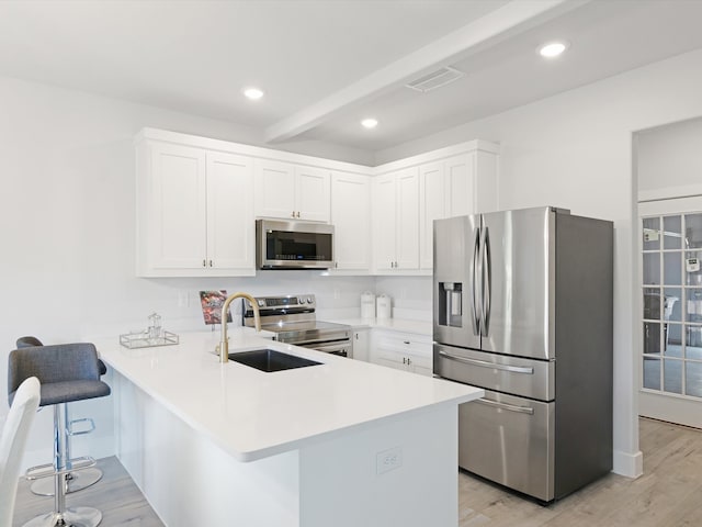 kitchen with stainless steel appliances, kitchen peninsula, a breakfast bar, white cabinetry, and light hardwood / wood-style flooring